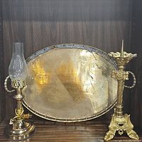 Lot displayed together showing an oval brass handled tray, a vintage brass hurricane lamp, and a brass pricket candlestick holder.