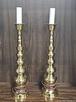 Pair of tiered brass table lamps with coiled cords at the base on wood surface against wood background.