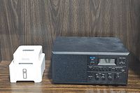 Vintage KLH 100 AM/FM clock radio next to Sonos ZoneBridge and Sonos Connect devices on wooden surface.