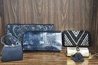 Photo showing 5 evening bags: black floral lace clutch, blue textured leather clutch, black/gold/silver beaded clutch, gold clutch with tassel, small black handbag.