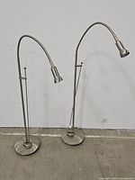 Both steel floor lamps side by side showing adjustable gooseneck heads and round weighted bases.