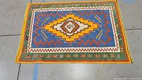 Overhead view of full rug, showing blue field, yellow central medallion, green border on concrete floor