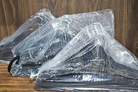 Three bundles of new black velvet hangers wrapped in clear plastic, showing multiple hangers with metal hooks in each bundle, set against a wooden background.