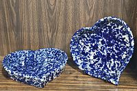 Pair of heart shaped stoneware dishes with blue and white speckled pattern placed side by side on a wooden surface.