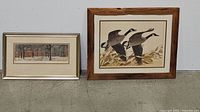 Two smaller framed artworks setting on floor: one depicting flying Canada Geese, the other an outdoor scene under trees.