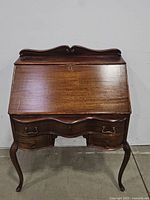Front view of antique secretary desk with closed drop-front writing surface and visible drawers and cabriole legs