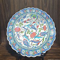 Front view of large round handmade porcelain decorative plate with colorful floral and bird motifs and scalloped edges