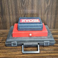 Three stacked tool cases: large black case (socket set), smaller red Swingline power stapler case, small blue Ryobi drill bits case on top