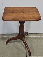 Full view of the vintage wooden pedestal table showing its rectangular top and three curved legs.