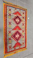 Full view of rectangular orange, yellow and red Moroccan woven rug with geometric and cross patterns, laid flat on floor.