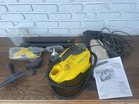 Full lot overview showing Eureka Enviro Multi Steamer, accessories, manual, and carry bag on wooden surface