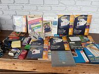 Photo showing multiple unopened and some opened Avery label packages, glossy photo paper, photos of inkjet paper, and various office paper products spread on wooden surface.