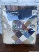 Quilt folded in packaging showing patchwork design with label indicating the product name Kaleidoscope Quilt and showcasing the various patterned fabrics in cream, blue, brown, green, and floral colors.