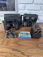 Overall view of five pairs of binoculars on wooden table including cases and a boxed pair of sports binoculars.