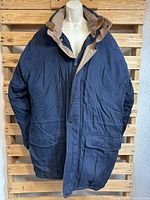 Front view of the men's dark down coat with tan inner lining on neck and hood, displayed on mannequin.