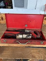 Milwaukee Sawzall reciprocating saw inside sized red metal carrying case, cord coiled with saw.
