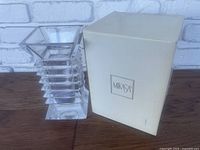 Mikasa Maka Pagoda style clear lead crystal square vase with original box placed beside it on wooden surface against white brick background.