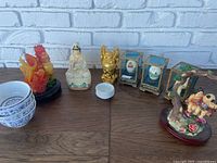 Overview of all items in the mixed oriental lot showing dragon sculpture, Guanyin and Buddha statues, three eggs in display cases, four bowls stacked, and swinging children figurine