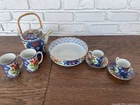 Full tea set with teapot, serving bowl, tea cups and saucers, and coffee cups arranged on wooden surface