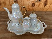 Full view of the tea set on tray showing teapot, creamer, sugar bowl with lids and gold accents