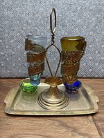 Photo showing silver plated tray with removable stand holding four colored glass vessels in blue, green, amber, and clear glass.