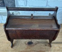 Front angled view of the vintage wooden sewing box showing the handle, lid, and carved feet.