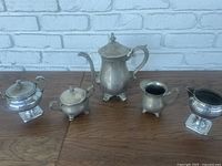 Full view of four piece vintage brass tea set on wood surface against white brick background.