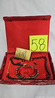 Jewelry set displayed inside red embroidered box with matching red interior lining. Includes necklace, bracelet, and earrings along with original collection tag.