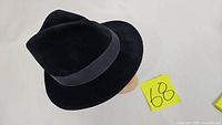 Black wool fedora hat shown on a model head, with a wide black band and classic fedora shape.