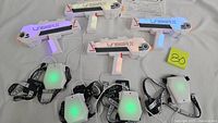 Four Laser X blasters in white and black colors with LED light features, and four chest target sensors with lanyards, laid out on white background. Instruction manual positioned above blasters.