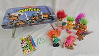 Photo showing Teenage Mutant Ninja Turtles metal TV tray with foldable legs, 12 Troll Dolls with colorful hair, and Mickey Mouse-themed ballpoint pens.