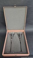 Open box showing two crystal champagne flutes inside, cushioned fitted interior protecting the glasses.