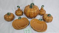 Photo showing all items including one large pumpkin tureen, four small lidded serving bowls, and pumpkin-shaped plates arranged in front.
