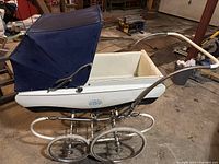 Side view of antique Pedigree baby carriage showing navy blue fabric canopy, white wooden body, and metal frame with large spoked wheels.