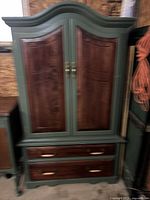 Front view of armour green wooden cabinet with darker wood panel doors and two drawers below