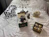 Overview of all holiday items on a bed including mugs, sleigh, candles, Nativity candle holder, and bulb ornaments.