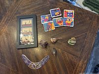 Lot contents on wooden table including framed print, boomerang, magnets, and carved figurines
