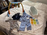 Full lot overview including baby tub, toy arch, baby clothes, and bottles on bed
