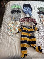Selection of assorted baby clothing including bodysuits, footed pajamas, and sleep sack spread out on a white surface.