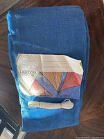 Folded blue shade sail with attached instruction leaflet and mounting rope on top.
