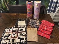 Photo showing all items including two rolls of gift wrapping paper and assortment of handmade fabric and paper gift bags arranged on table.