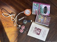 Top view of the hiking books including official Bruce Trail guide, other hiking and culinary books, along with a stop watch, compasses, whistle, and a mechanical km tracker.