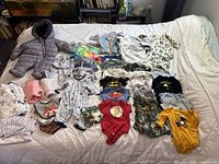 Photo showing full assortment of infant wear laid out on bed including snowsuit, onesies, and socks