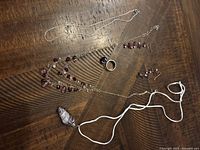 Overview of the jewelry set spread out on a wooden surface: necklace with pendant on white cord, earrings with purple beads, and ring with matching bead.