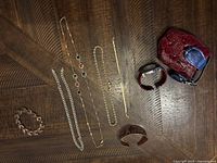 Wristwatch, red textured case, three bracelets, and three necklaces laid out on wood surface