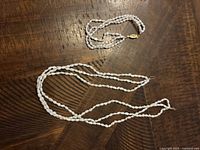 Pearl necklace laid out on wooden surface, showing strand and clasp.