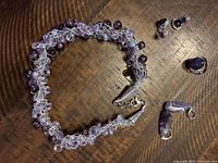 Purple beaded necklace with silver-colored wire and clasp, two sets of earrings, and a purple ring on wooden surface