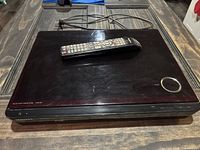 Top view of Samsung Blu-ray home theater system HT-BD1255 main unit showing remote control on top and power cord at backside.