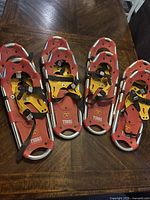 Four pairs of red Tubbs snowshoes with yellow bindings arranged on table