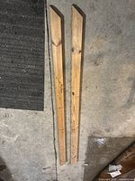 Two solid wood railings side by side on a concrete floor showing their length, shape, and condition.